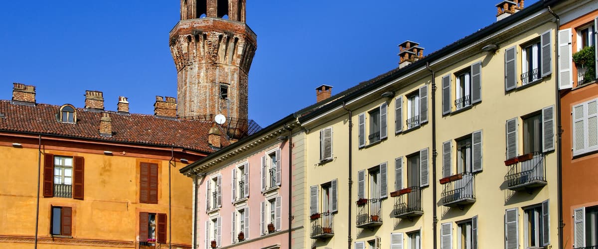 A historic tower with arched windows and a bell tower, surrounded by colorful buildings with balconies and shutters.
