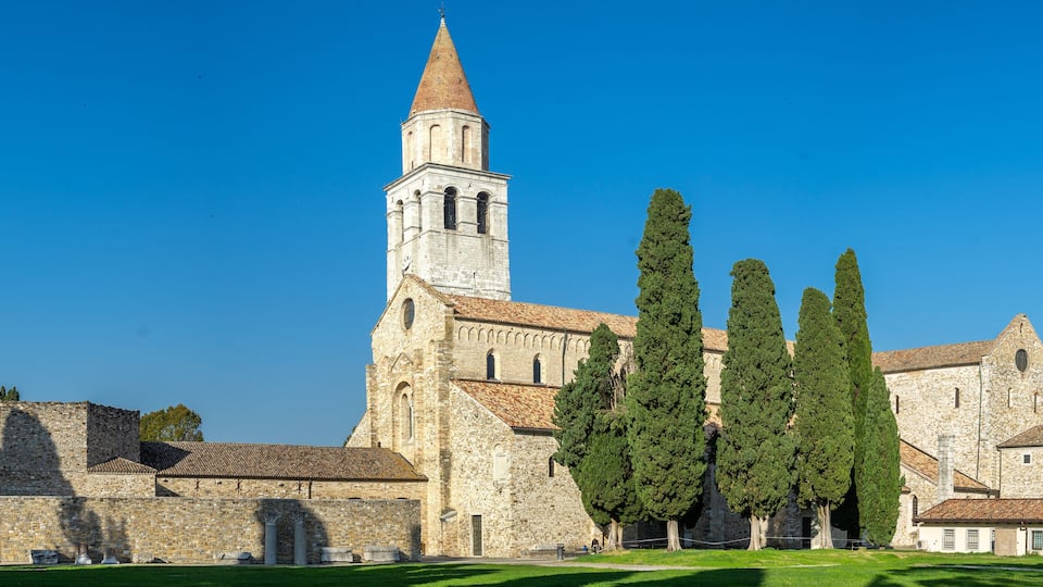 A historic church with a tall bell tower, surrounded by tall cypress trees.