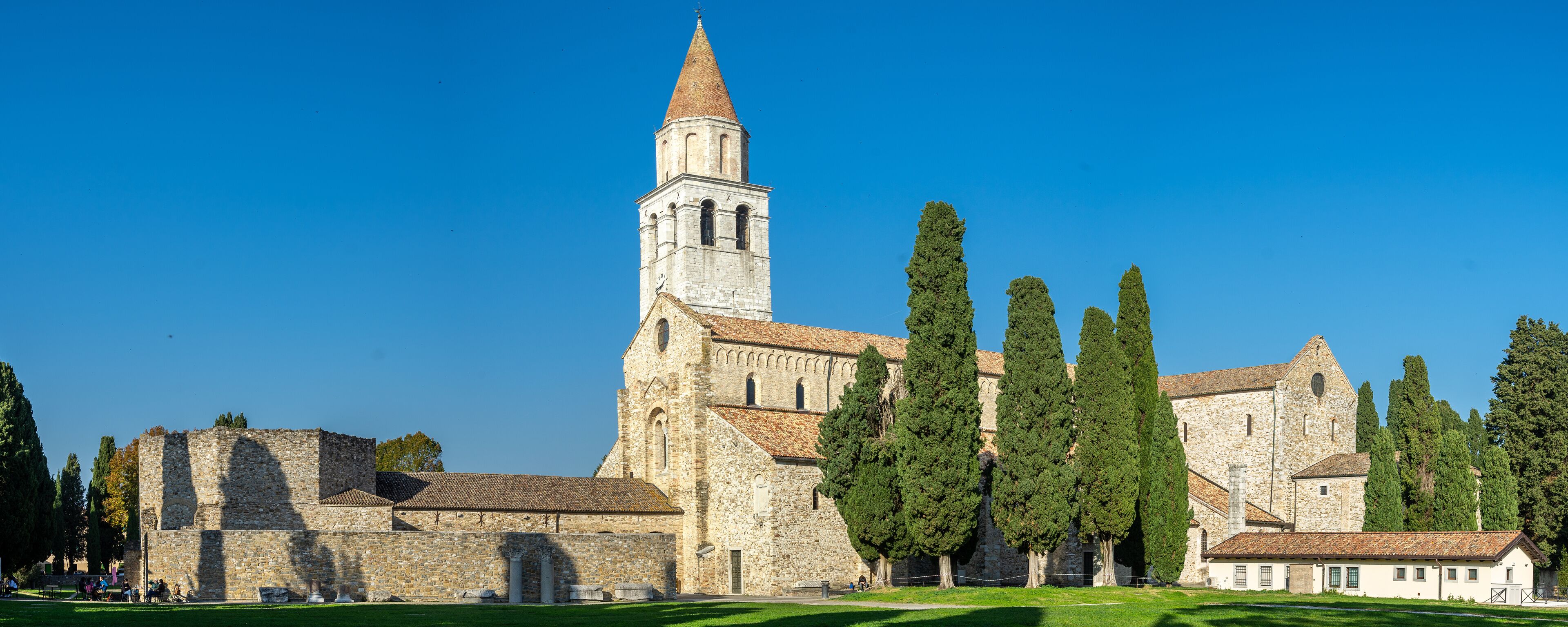A historic church with a tall bell tower, surrounded by tall cypress trees.