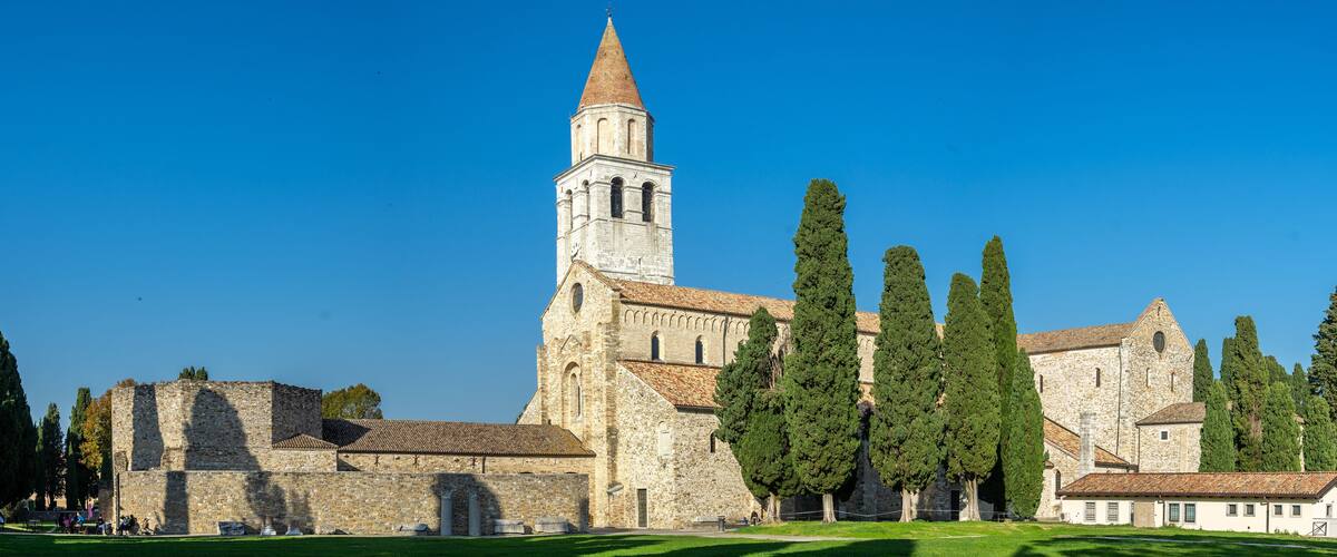 A historic church with a tall bell tower, surrounded by tall cypress trees.