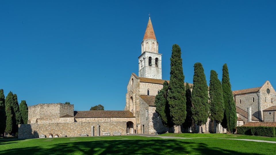 A historic church with a tall bell tower, surrounded by well-maintained greenery and ancient stone walls.