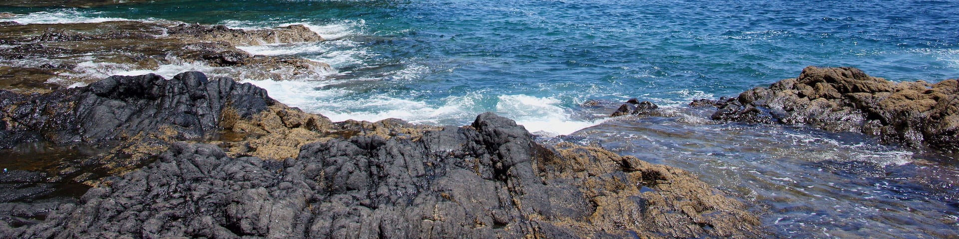 A rocky coastline with waves crashing against the shore and a steep cliff in the background.