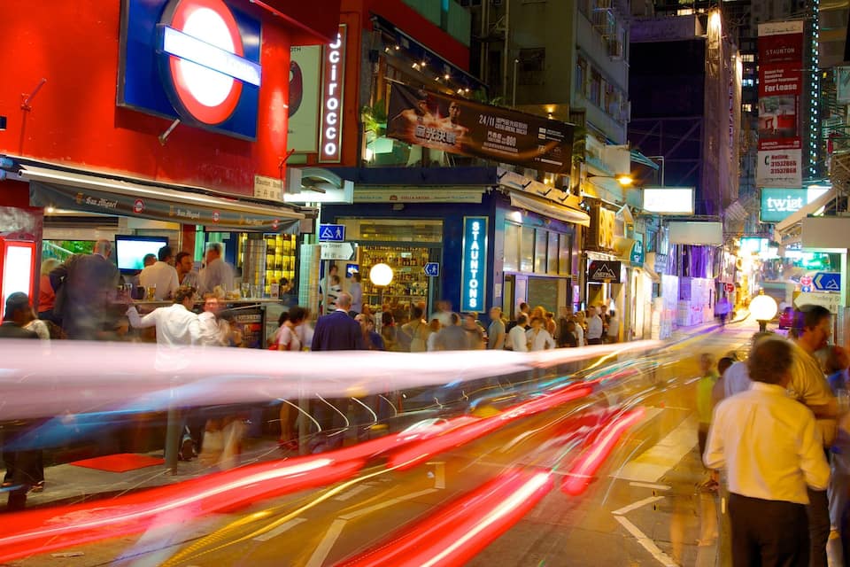A busy street with a red building featuring a prominent Tube station sign, a bar, and various shops.
