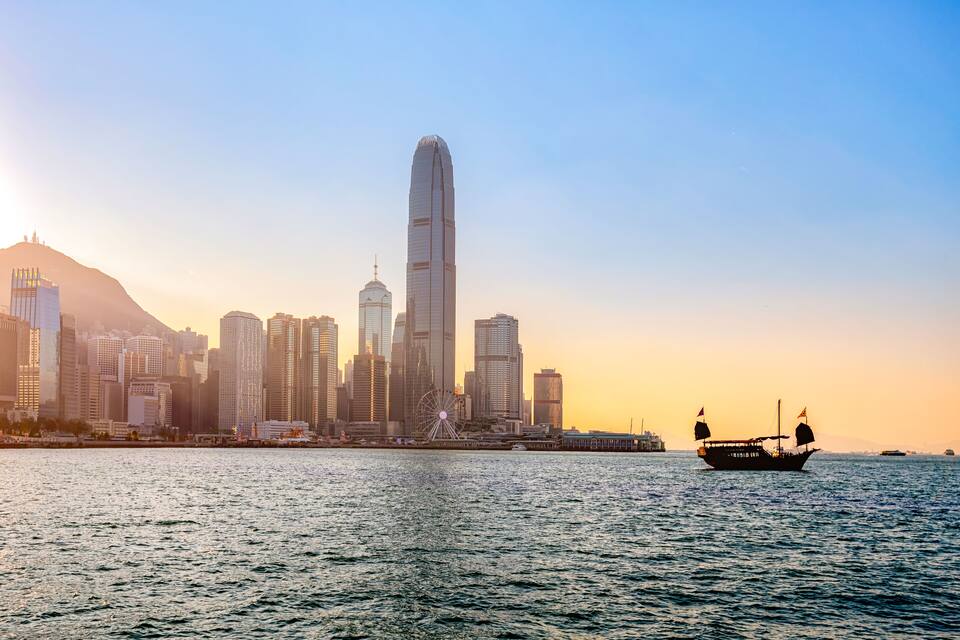 A city skyline with a prominent skyscraper, a Ferris wheel, and a boat on the water.