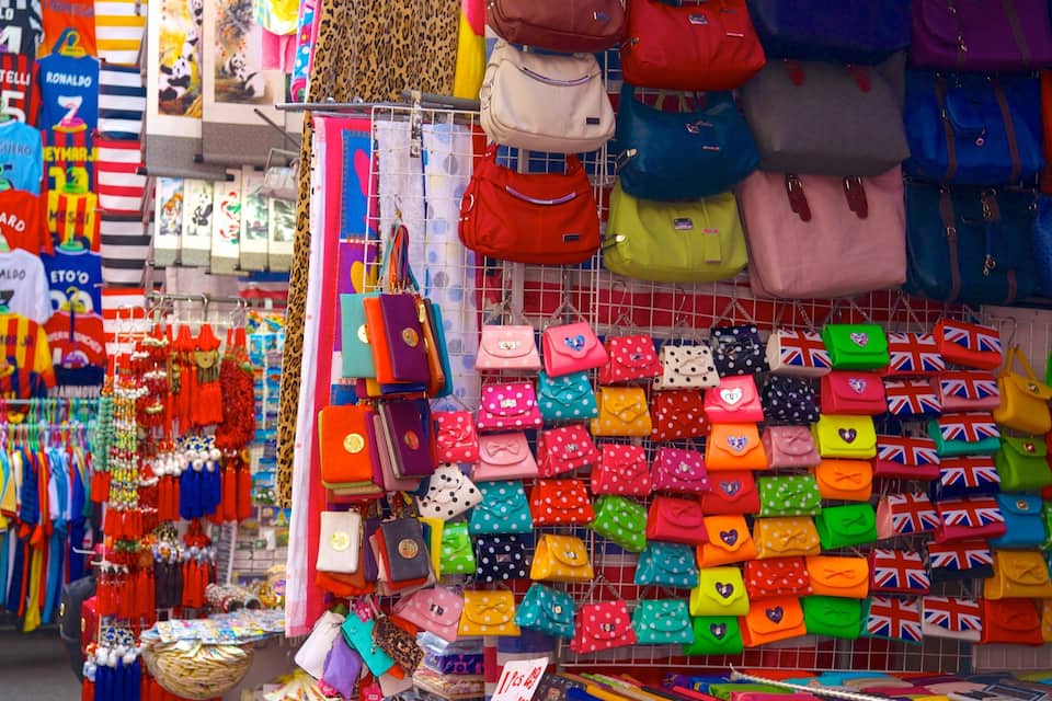 A market stall with colorful bags and sports jerseys.