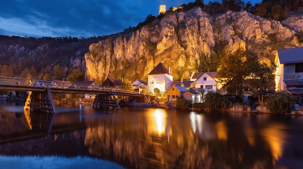 A river reflecting buildings and a bridge with a mountain backdrop.