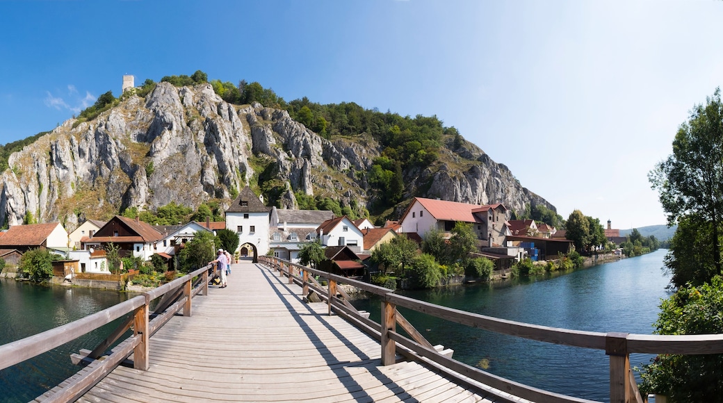A wooden bridge leading to a village with houses and a castle on a hill.