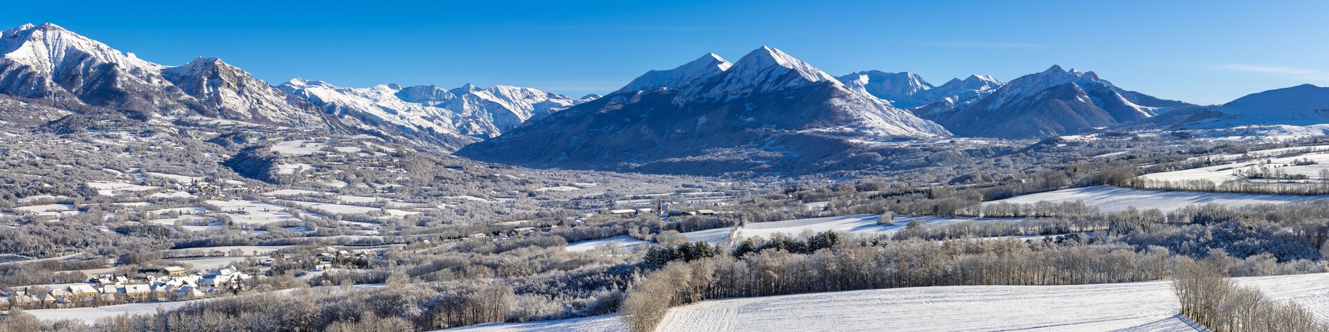 Paisagem montanhosa coberta de neve, com um vale e edifícios dispersos.