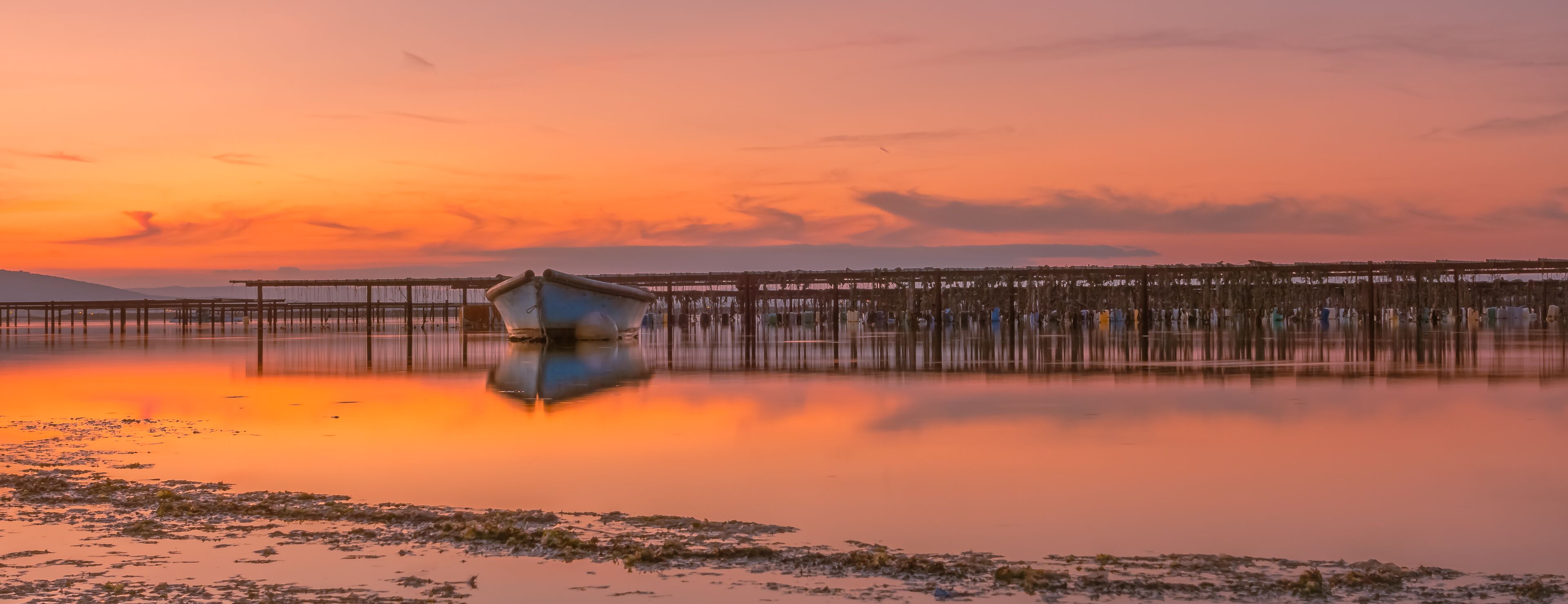 A sunset over a calm lake with a wooden pier extending into the water.