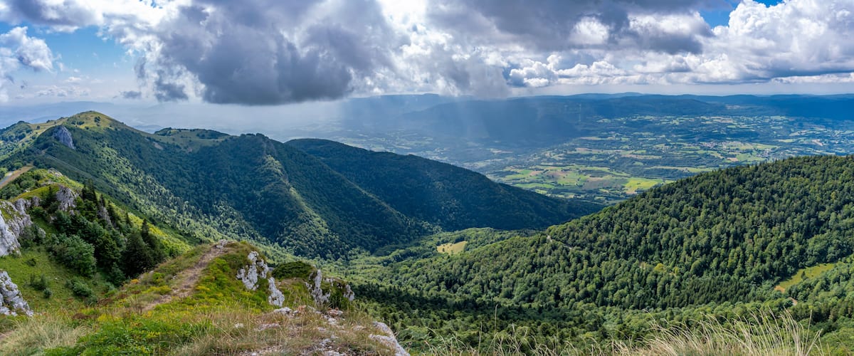A mountainous landscape with dense forests, a winding path, and a valley below.