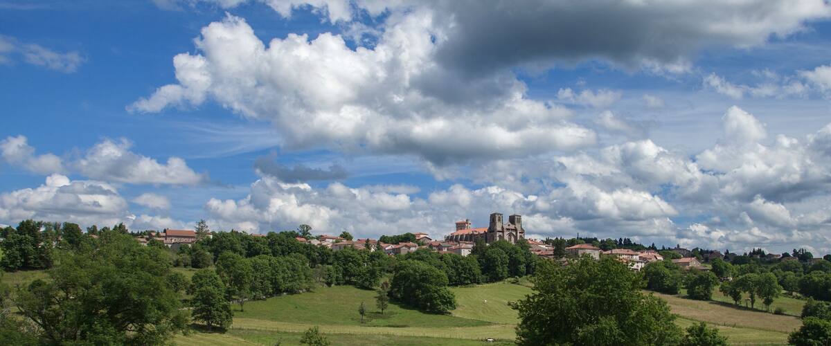 A town with a prominent church on a hill, surrounded by green fields and trees under a partly cloudy sky.