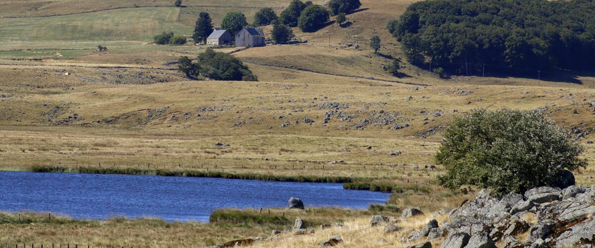 A rural landscape with a lake, rolling hills, a barn, and scattered trees.