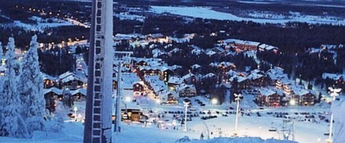 A snow-covered ski resort at dusk with illuminated buildings and a ski lift.
