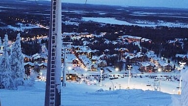 Estación de esquí cubierta de nieve al anochecer, con edificios iluminados y un telesilla.