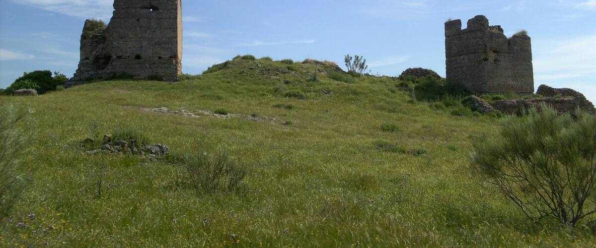 Two ancient stone ruins on a grassy hill under a clear sky.