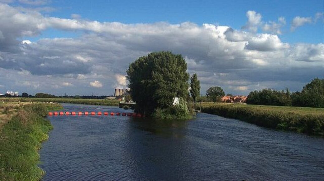 Beal- The River Aire. This photograph is taken from the Bridge over the River Aire at Beale, looking west. Eggborough Power Station can be seen on the horizon. The river is not navigable to the left of the island in the picture. There is a weir. To the right of the island is navigable via a lock.