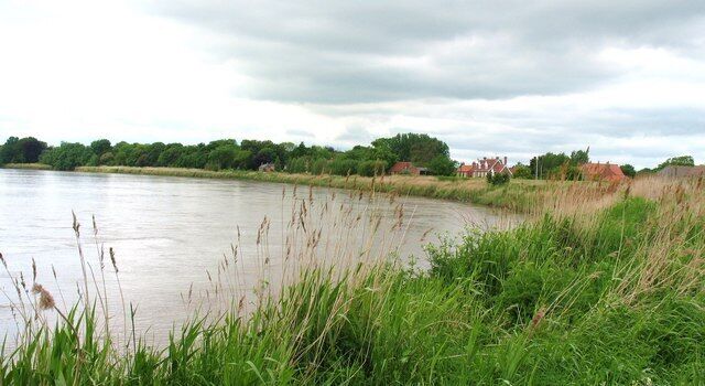 A river with grassy banks and houses in the background.