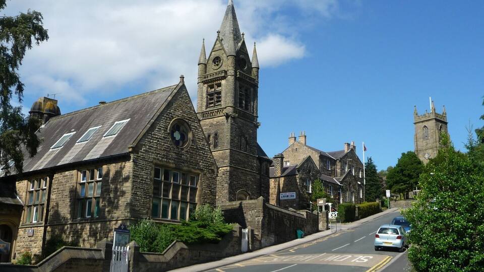 A historic stone church with a tall tower and a smaller steeple, set in a quaint village with narrow roads and traditional stone buildings.