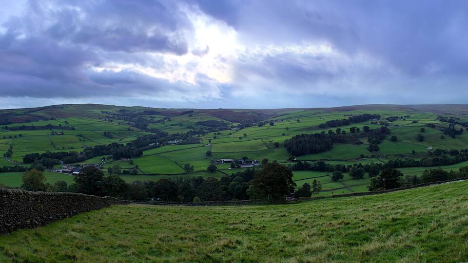Rolling green hills, stone walls, and a cloudy sky.