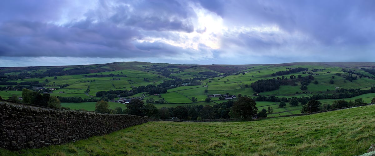 Rolling green hills, stone walls, and a cloudy sky.