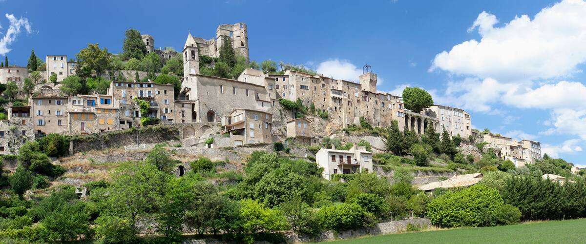 A historic town with stone buildings perched on a hillside, surrounded by greenery.