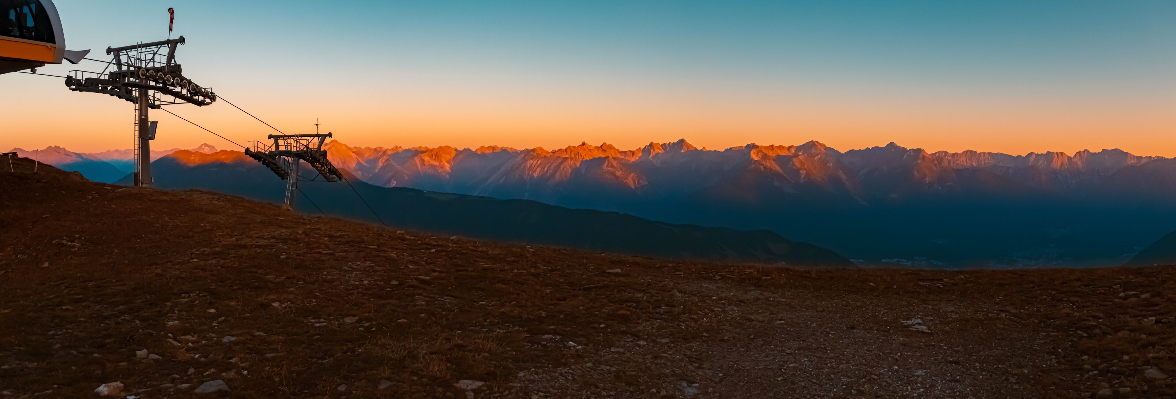 A ski lift at sunset with mountain peaks in the background.