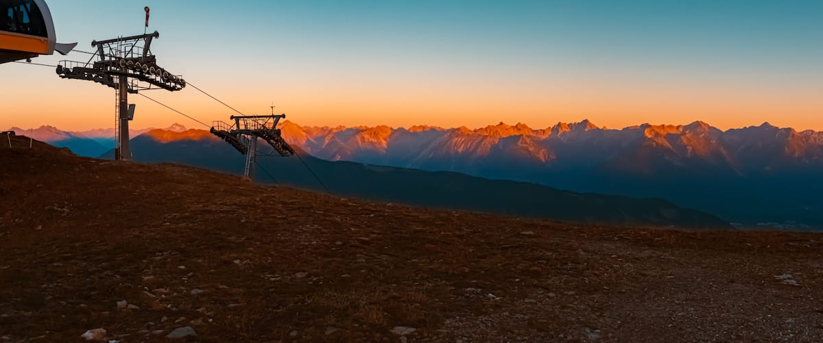 A ski lift at sunset with mountain peaks in the background.