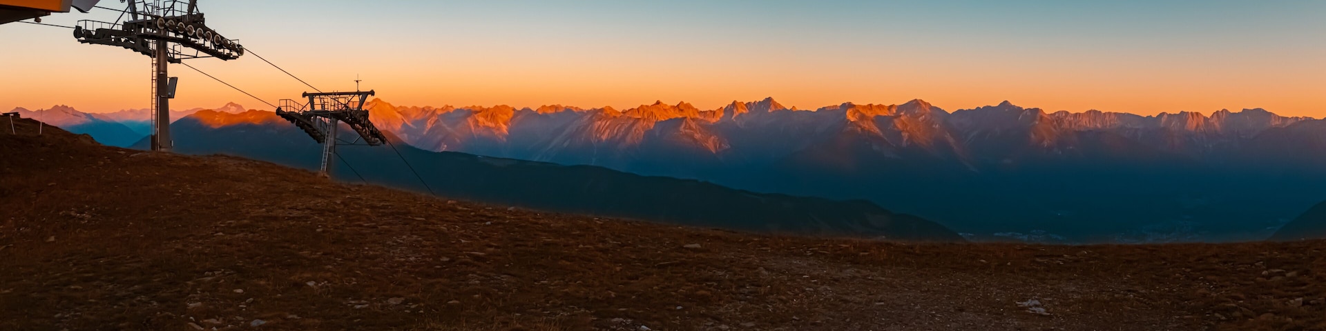 A ski lift at sunset with mountain peaks in the background.