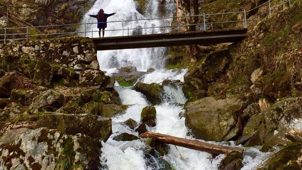A waterfall cascading over rocks with a bridge and a person standing on it.