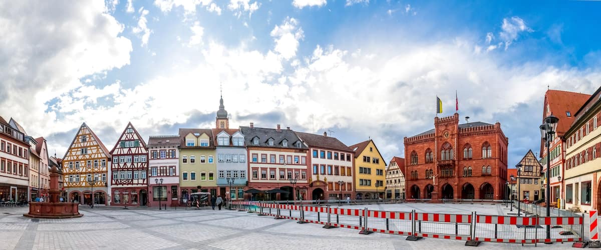 A historic European town square with colorful half-timbered buildings, a prominent church, and a fountain.