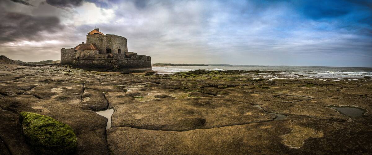 A coastal fortification with a round tower, surrounded by rocky terrain and the ocean.