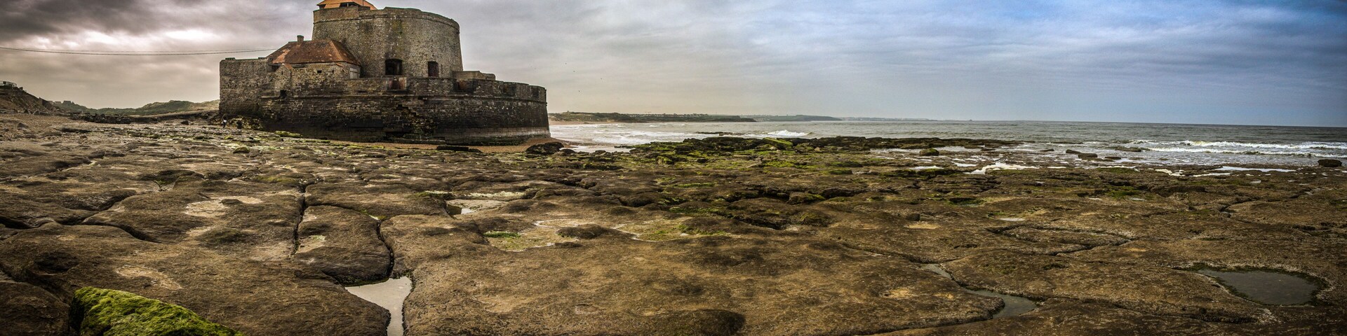 A coastal fortification with a round tower, surrounded by rocky terrain and the ocean.