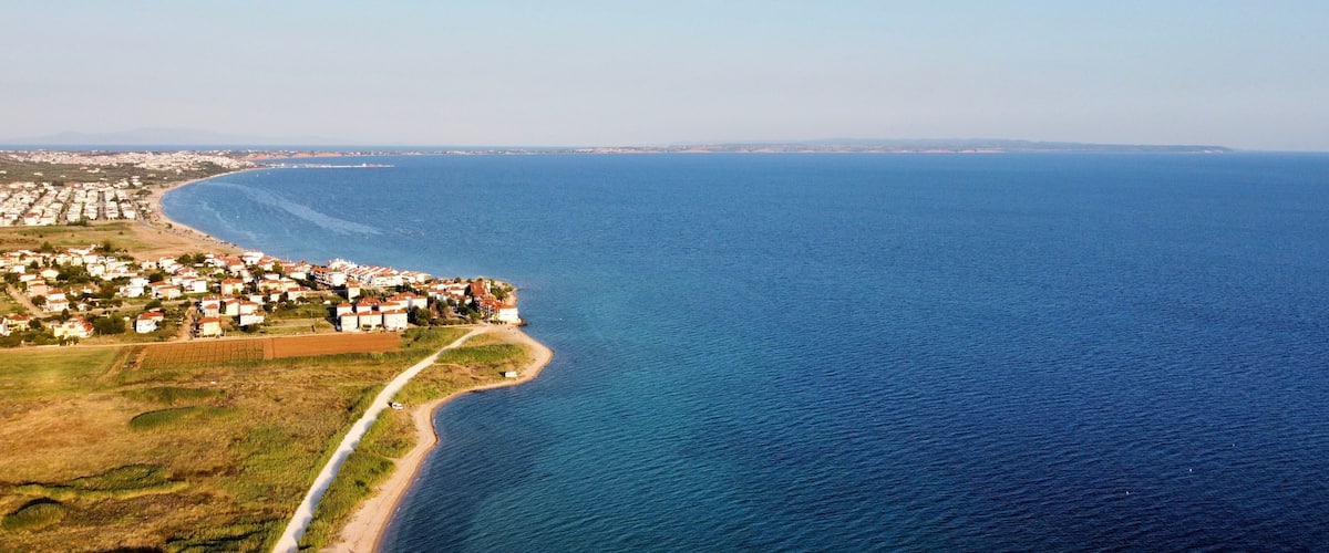 An aerial view of a coastal town with a beach, houses, and a clear blue sea.