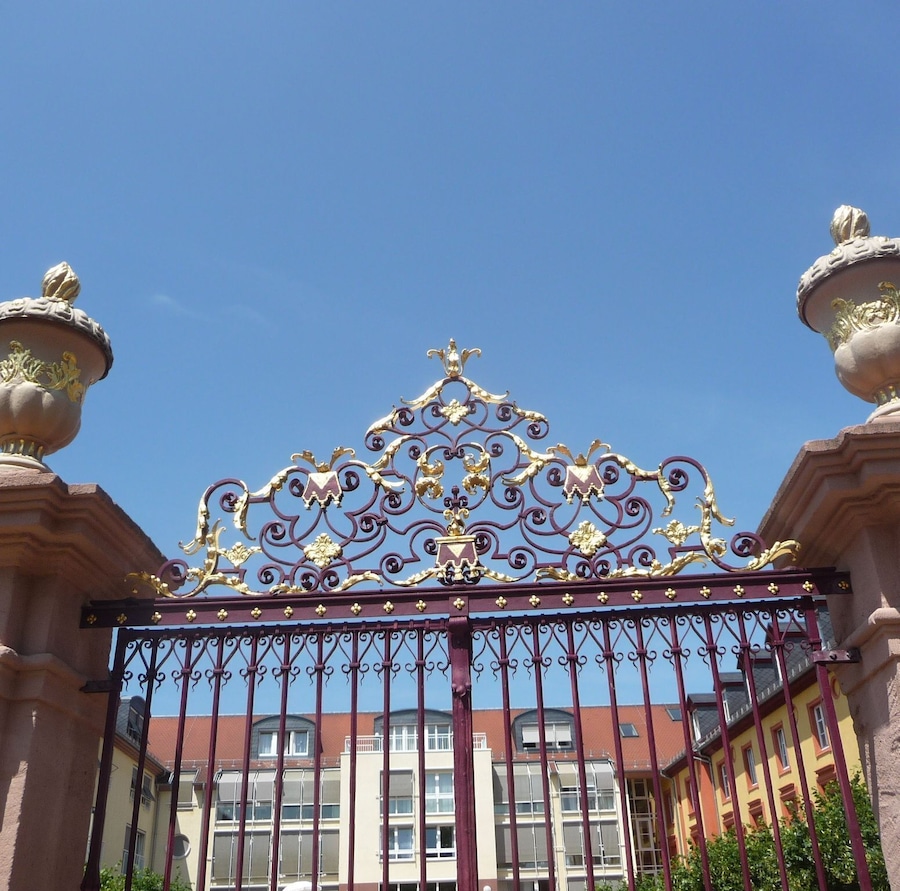 A wrought iron gate with ornate designs and two stone pedestals.