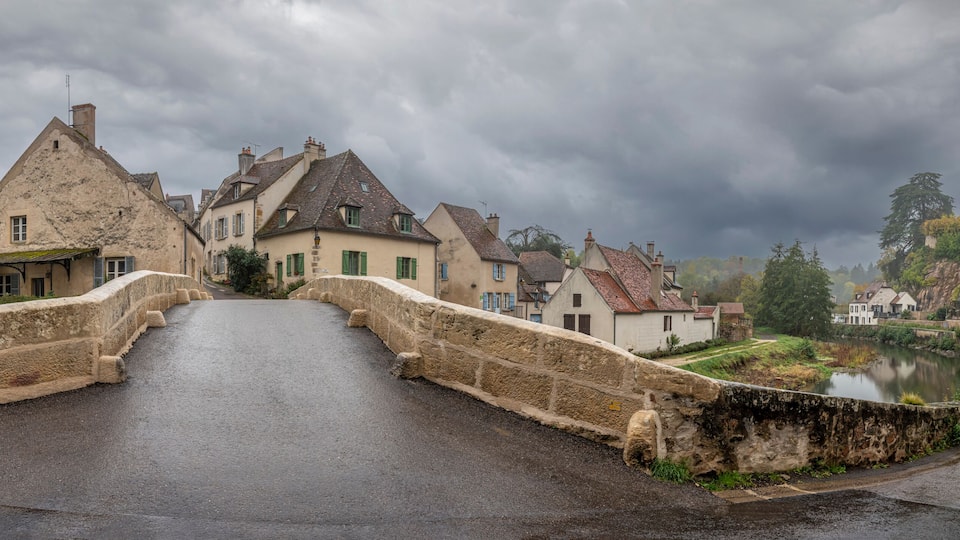 A stone bridge over a river in a historic town with old buildings and a castle in the background.