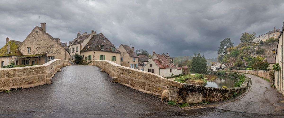 A stone bridge over a river in a historic town with old buildings and a castle in the background.