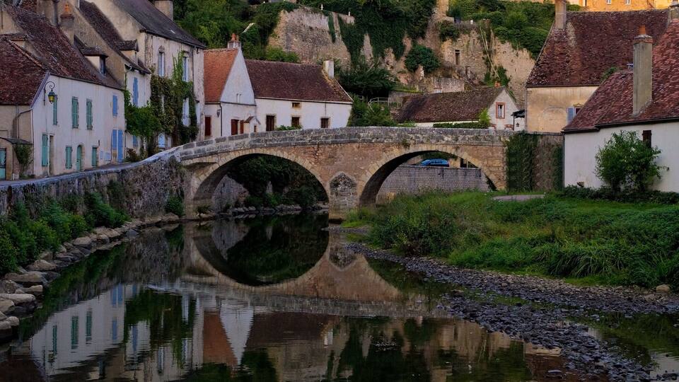A historic town with a river, a stone bridge, and a prominent church with a tall spire.
