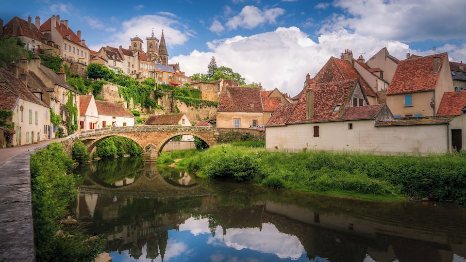 A historic town with a river, a stone bridge, and a church on a hill.