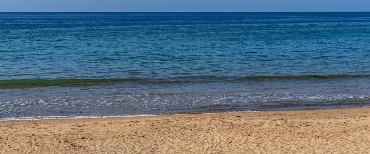 A beach with clear blue water and a sandy shore.