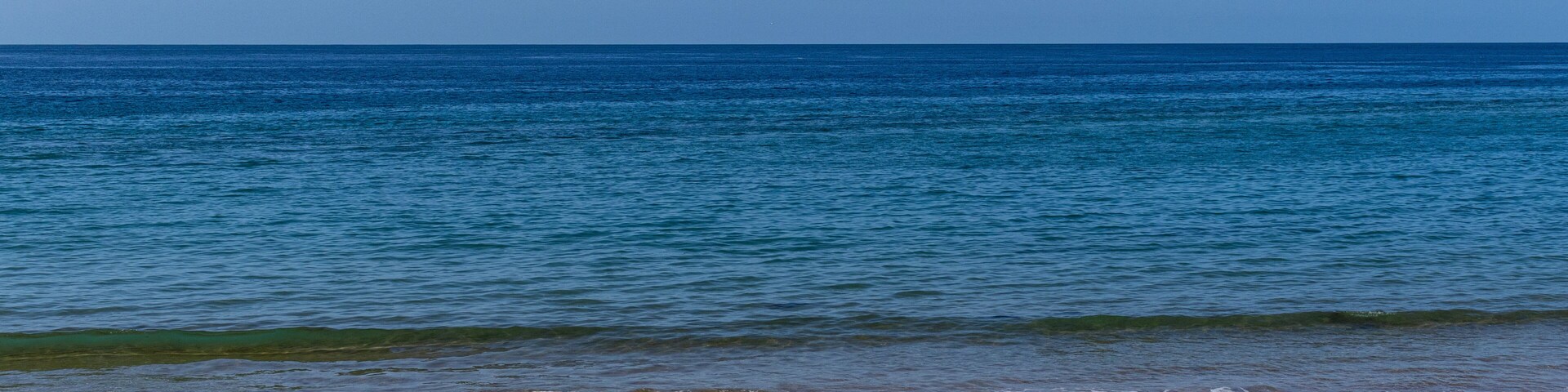 A beach with clear blue water and a sandy shore.