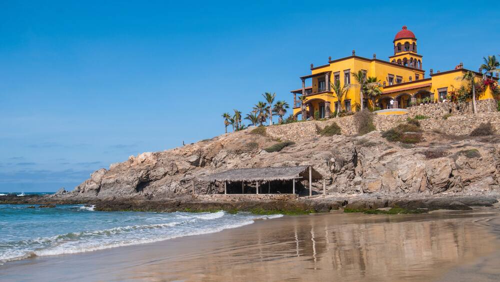A coastal building with a red dome, situated on a rocky hillside with palm trees.