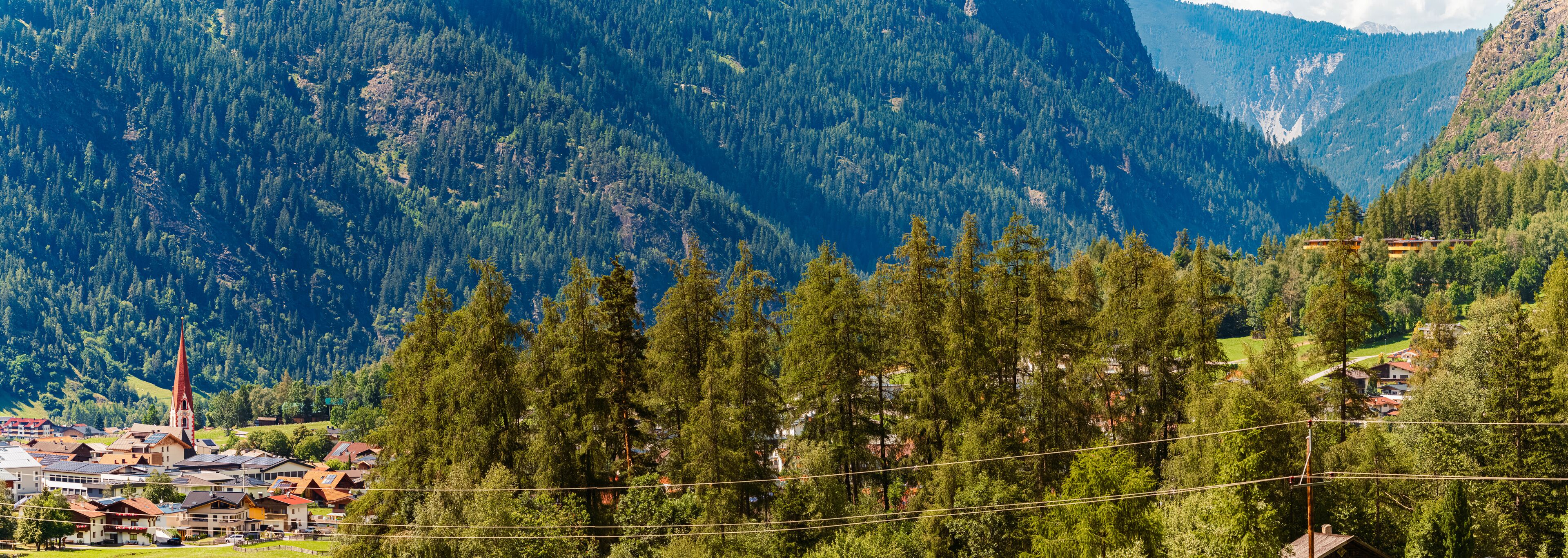 A mountainous landscape with dense forests, a church, and residential buildings.