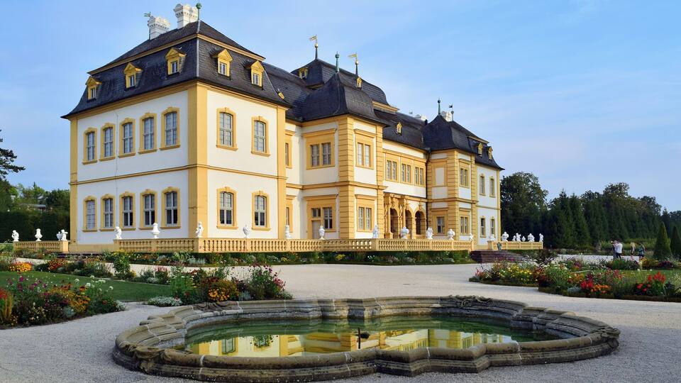 A large, historic building with a symmetrical facade, a central courtyard, and a fountain.