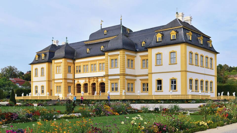 A large, yellow and white building with multiple windows and a garden in front.