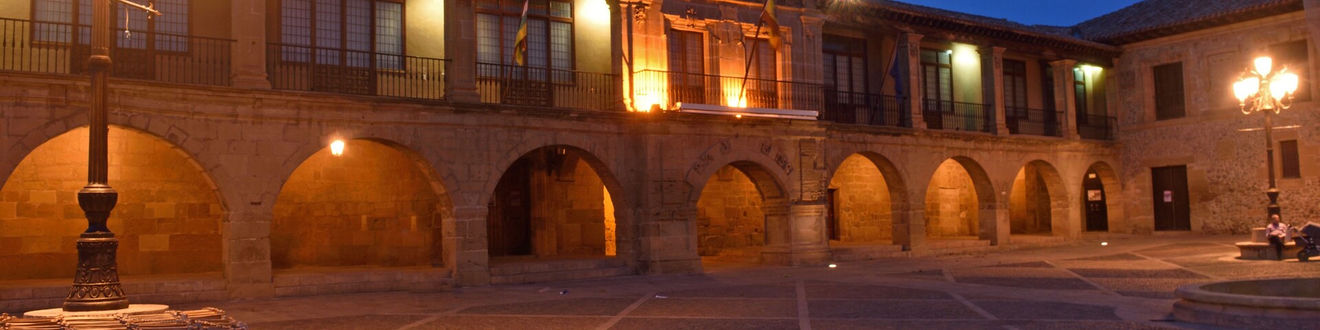 Un patio histórico con arcos, una torre del reloj y farolas.