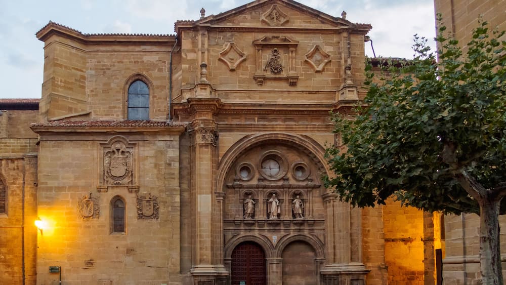A historic church with a large arched entrance, statues, and a cross on the roof.