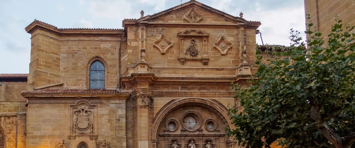 A historic church with a large arched entrance, statues, and a cross on the roof.