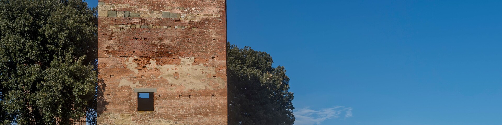 A historic brick tower with a narrow entrance, surrounded by trees and a modern sculpture.