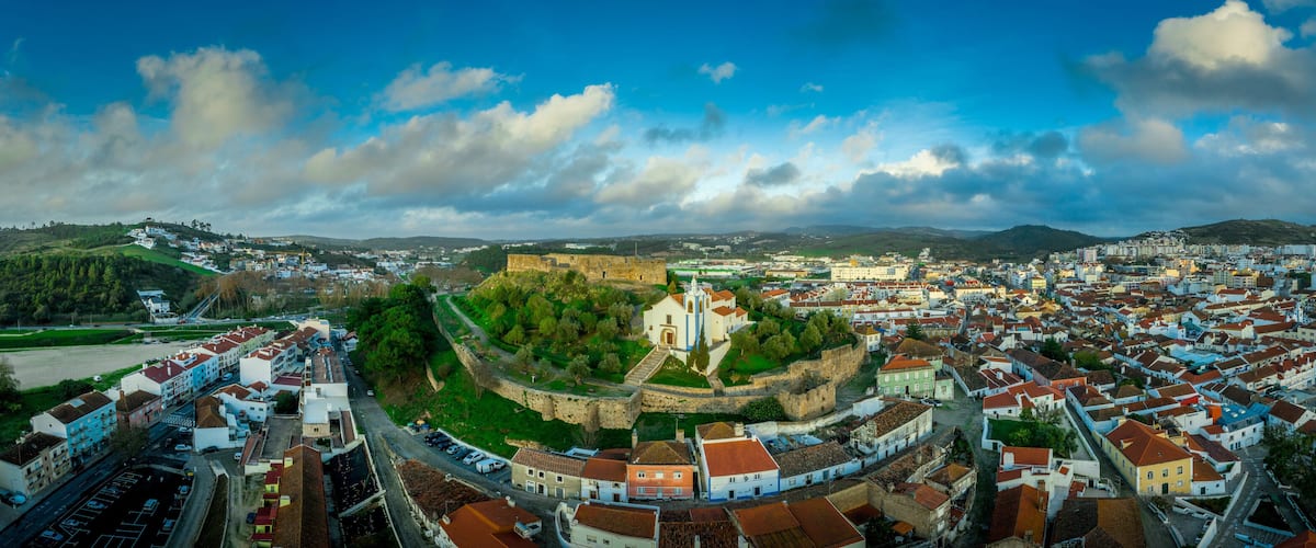 A panoramic view of a historic town with a prominent castle on a hill, surrounded by a dense urban area with traditional architecture.