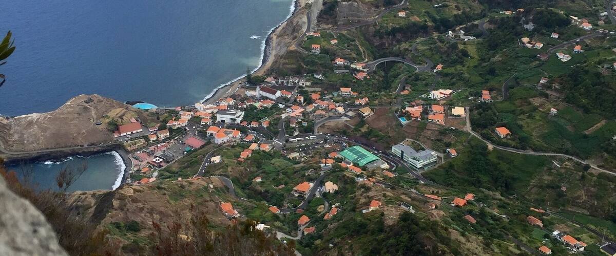 A coastal village with houses, a winding road, and a mountainous backdrop.